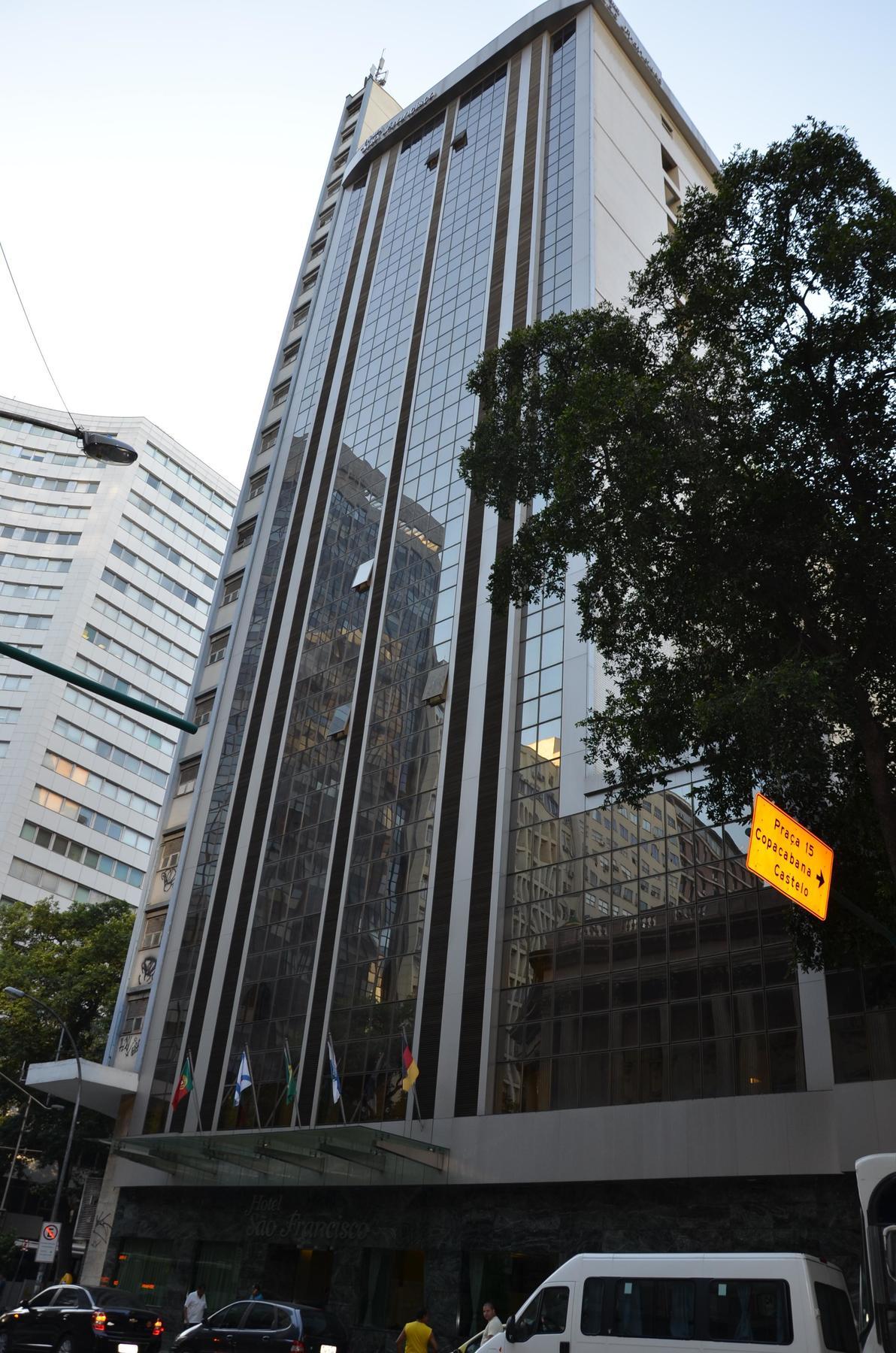 Hotel Atlantico Tower Rio de Janeiro Bagian luar foto The photo shows a city street with tall buildings. In the foreground, there is a modern glass skyscraper featuring reflective surfaces and vertical lines. Next to it, there's another building with a different architectural style, also made of glass. 
